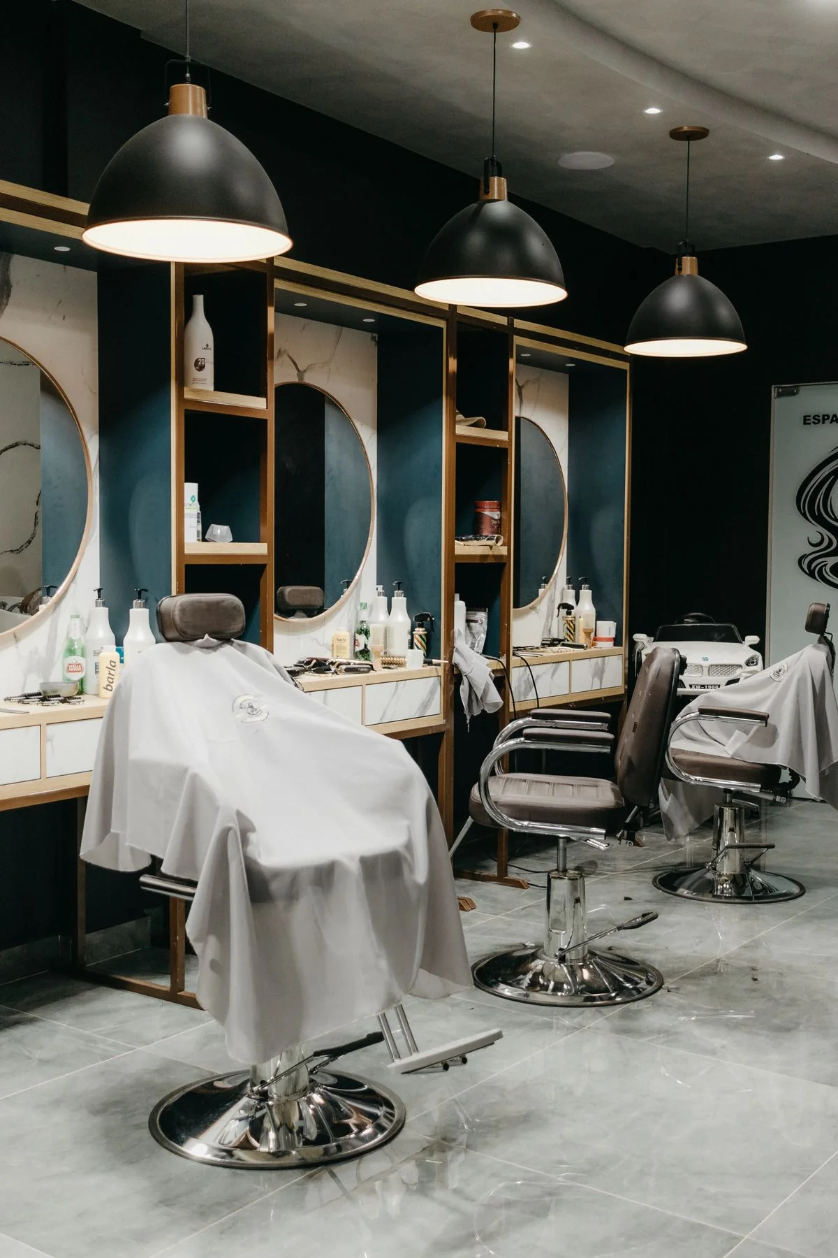Cadeiras e espelhos num interior de barbearia de tons escuros