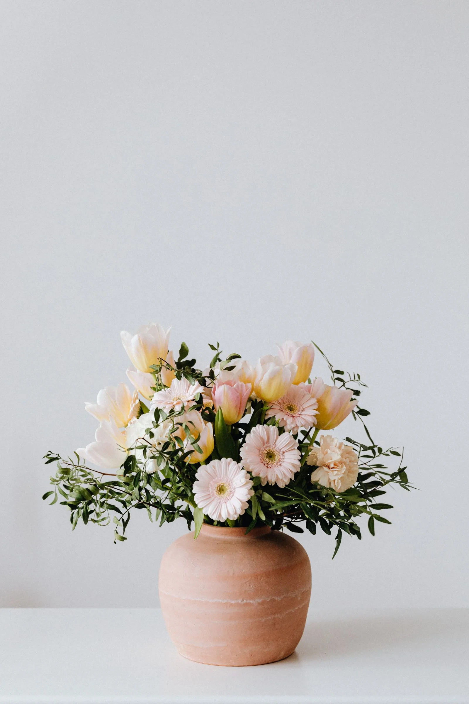 Composição de flores rosadas e amarelas num vaso claro